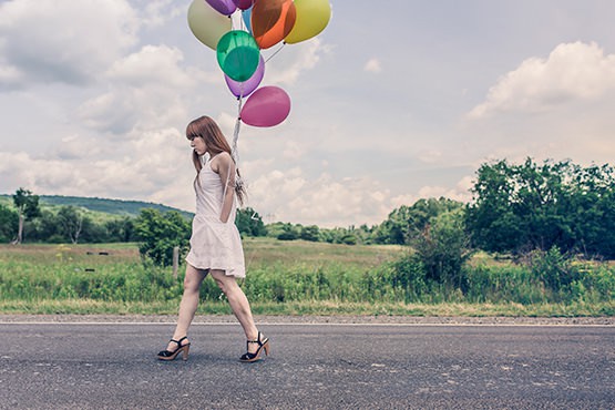 Foto van een vrouw die met ballonnen over straat loopt.